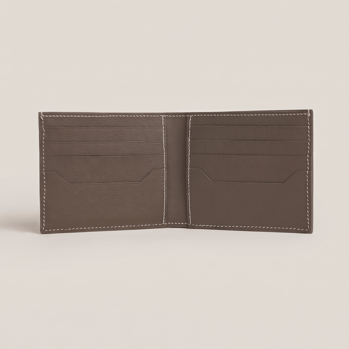 Fully opened interior of the bifold wallet in Étoupe French Alran goatskin, featuring eight card slots, two hidden slip pockets, and white hand stitching.