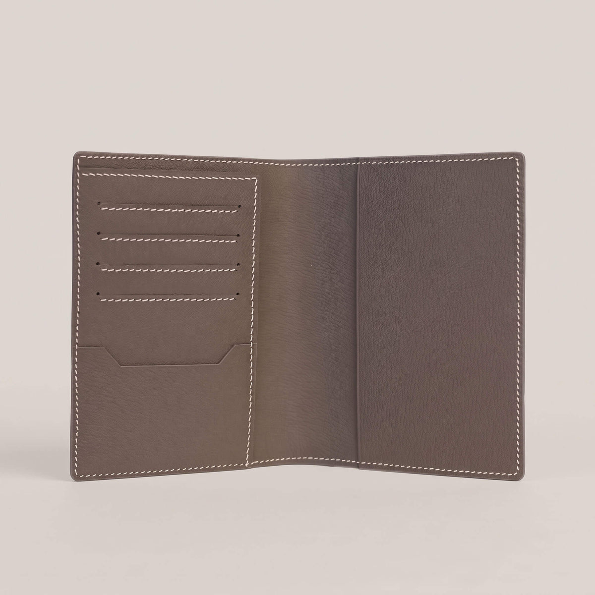 Fully opened interior of the passport wallet lined in Étoupe French Alran goatskin, featuring four card slots, an itinerary slip pocket, and contrasting white hand stitching.