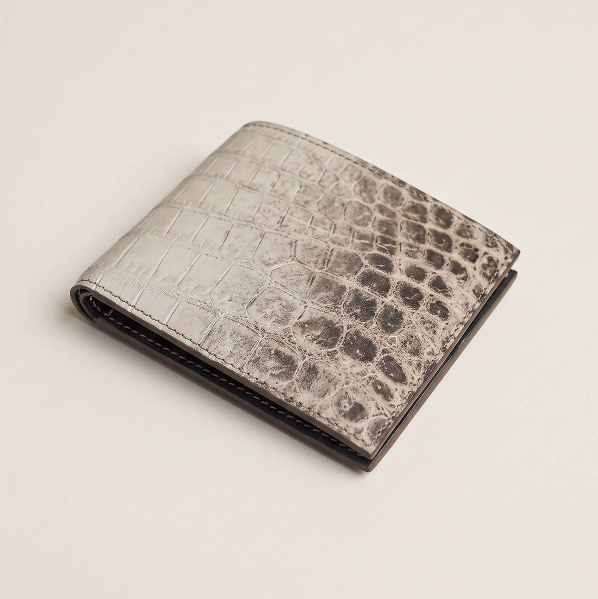Angled perspective of the closed luxury crocodile bifold wallet, showcasing its slim profile, spine folding curvature, and tactile matte patina.