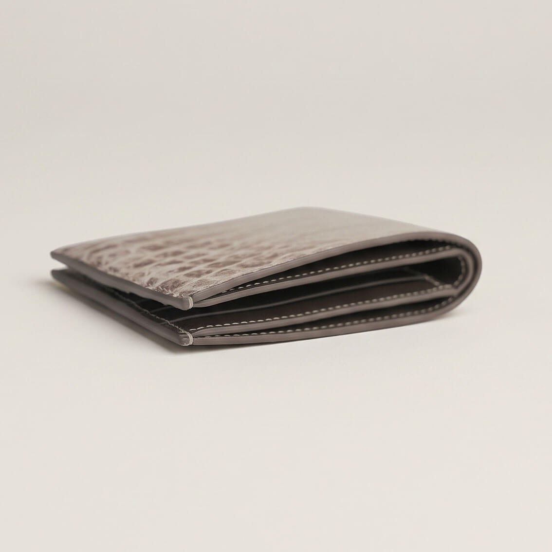 Side close-up view of the folded crocodile wallet, revealing the full-length currency compartment opening, layered edge coating, and saddle stitching.